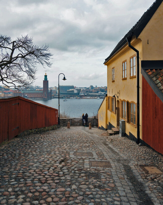 The view from Mariaberget. A yellow house on a cobbled street, with views leading down to the water and the City Hall on the other side.