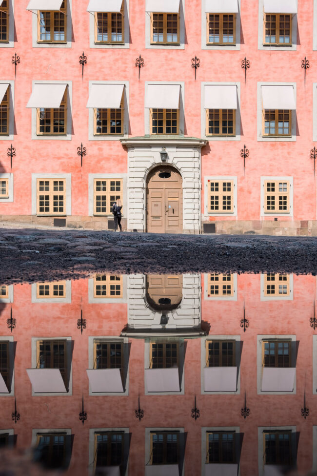 The pink exterior of Stenbock palaces, with a puddle reflecting the building.